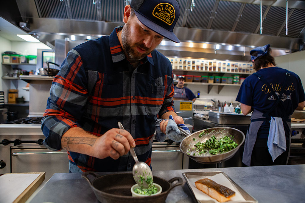 Minnesota Chef Erick Harsey spooning creamed spinach into a bowl for his gourmet salmon plate while sous chefs work in the background.