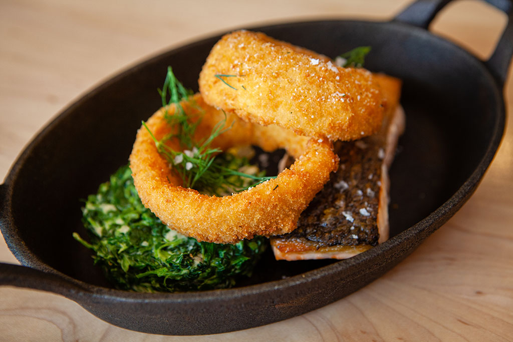 Salmon with creamed spinach and onion rings in a small cast iron skillet. Restaurant food products.