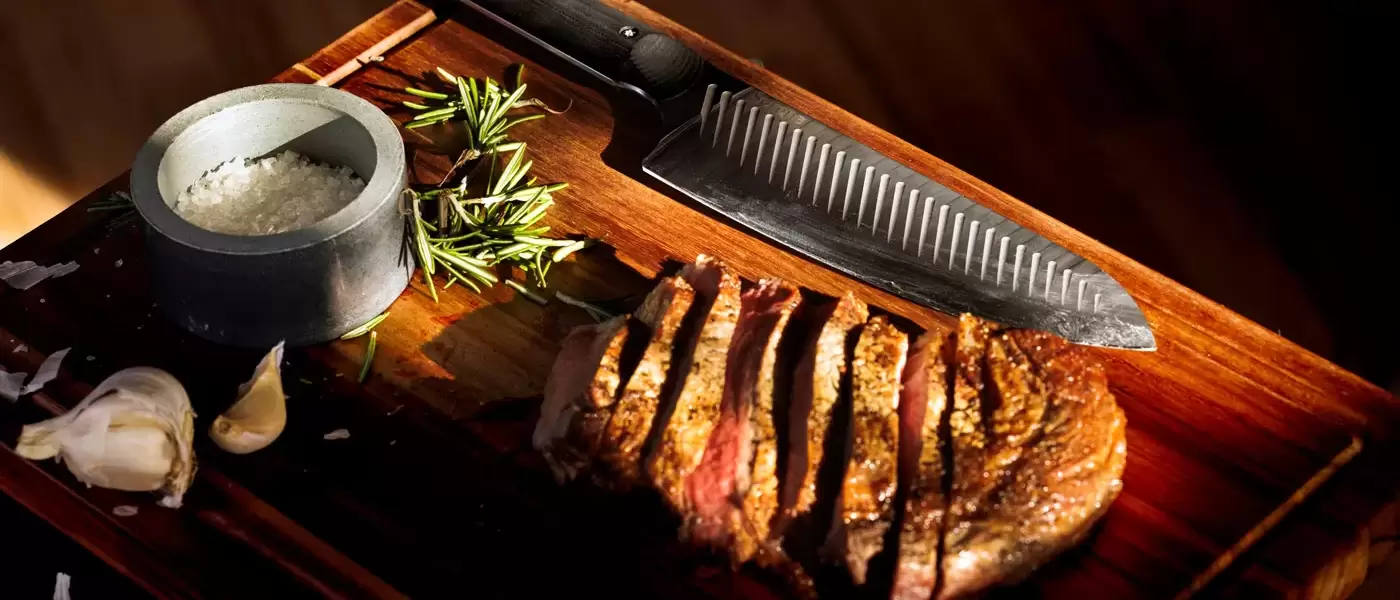 Product lifestyle photo of chefs knife with cut steak on a cutting board with herbs and coarse sea salt concrete cellar