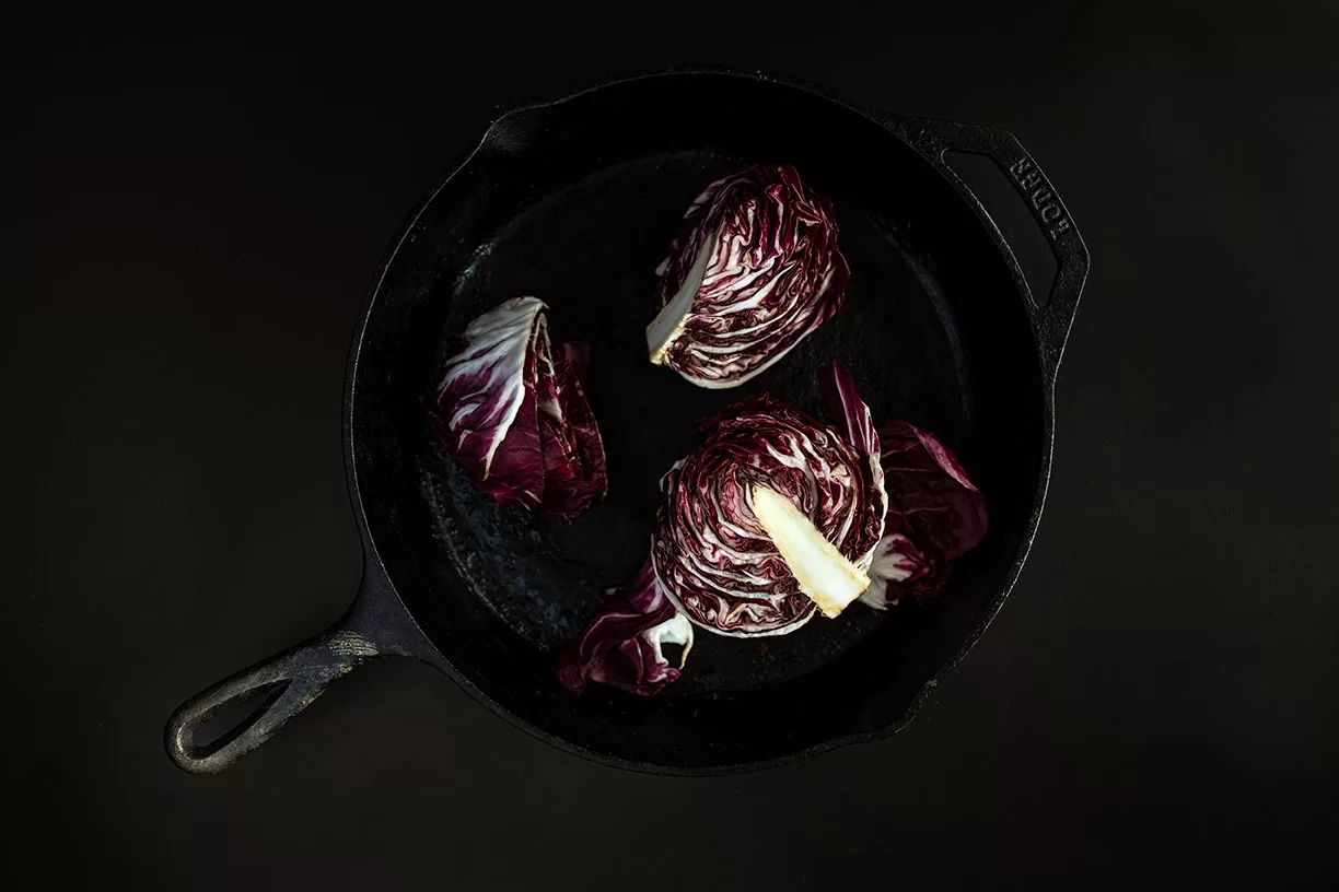 Radicchio cut into quarters set in a vintage cast iron pan with natural dark window light. Chicago commercial product photographer
